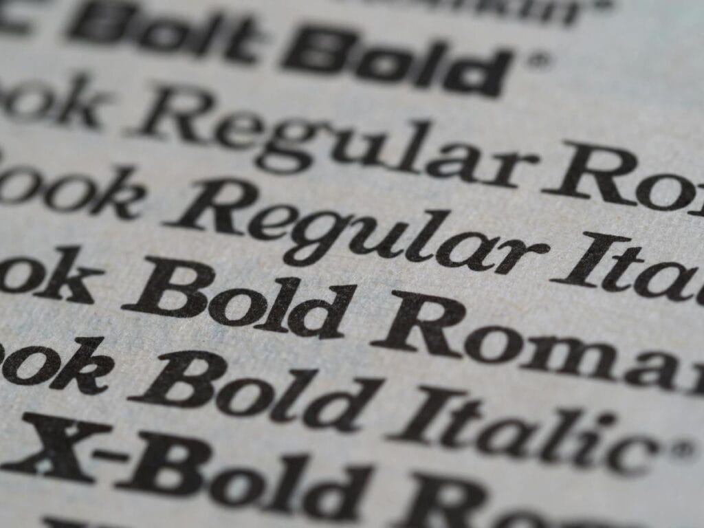 Close-up image showing printed font styles including 'Regular,' 'Italic,' 'Bold Roman,' and 'Bold Italic' on a textured paper background. The focus highlights the details of the font styles